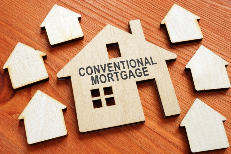 Wooden house cutout with "CONVENTIONAL MORTGAGE" text, surrounded by smaller house shapes on a wooden surface.
