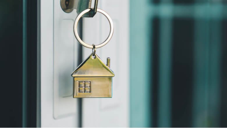 A brass house-shaped keychain hanging from a door key, symbolizing homeownership and new beginnings.