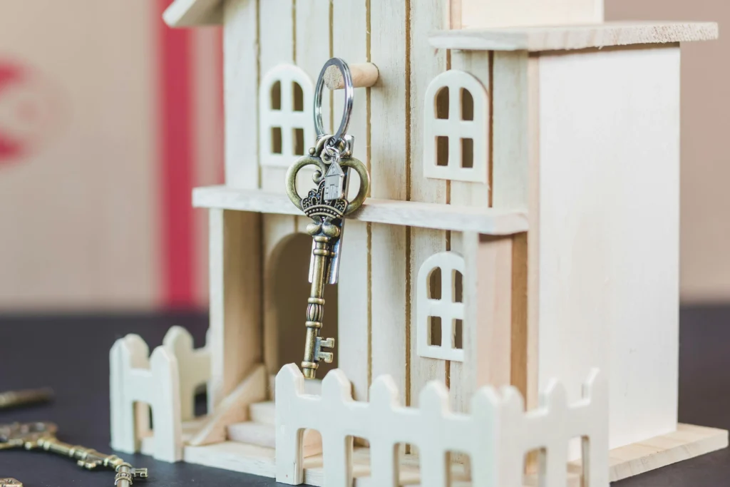 A decorative wooden house model with a keychain featuring a vintage-style key hanging from the entrance.