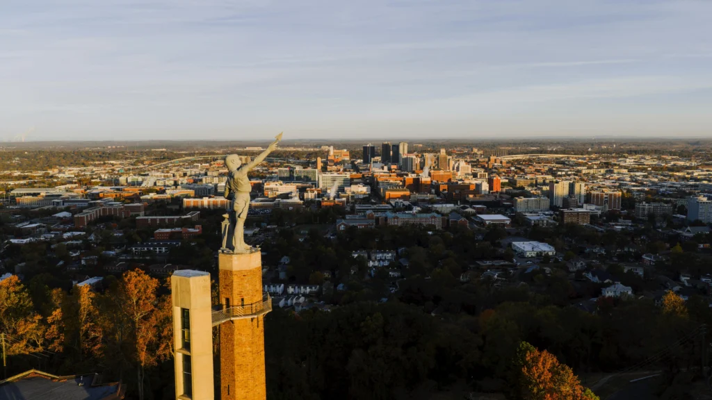 Aerial view of a city skyline featuring a prominent tower, with trees and buildings spread across the landscape at sunset.
