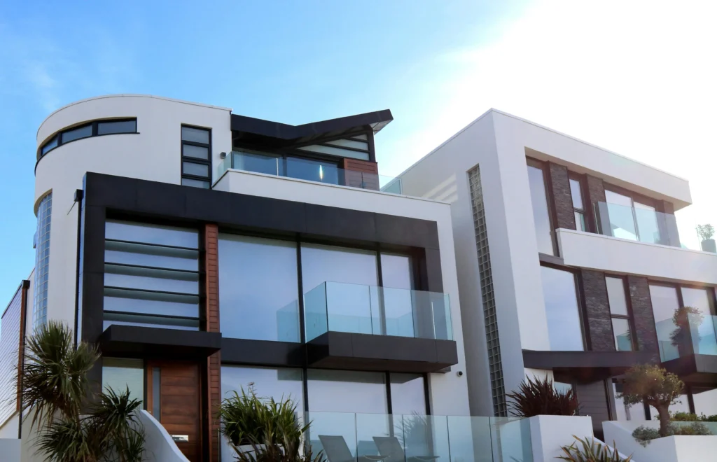 Modern architectural design featuring two sleek, white houses with large glass balconies and black accents under a clear blue sky.