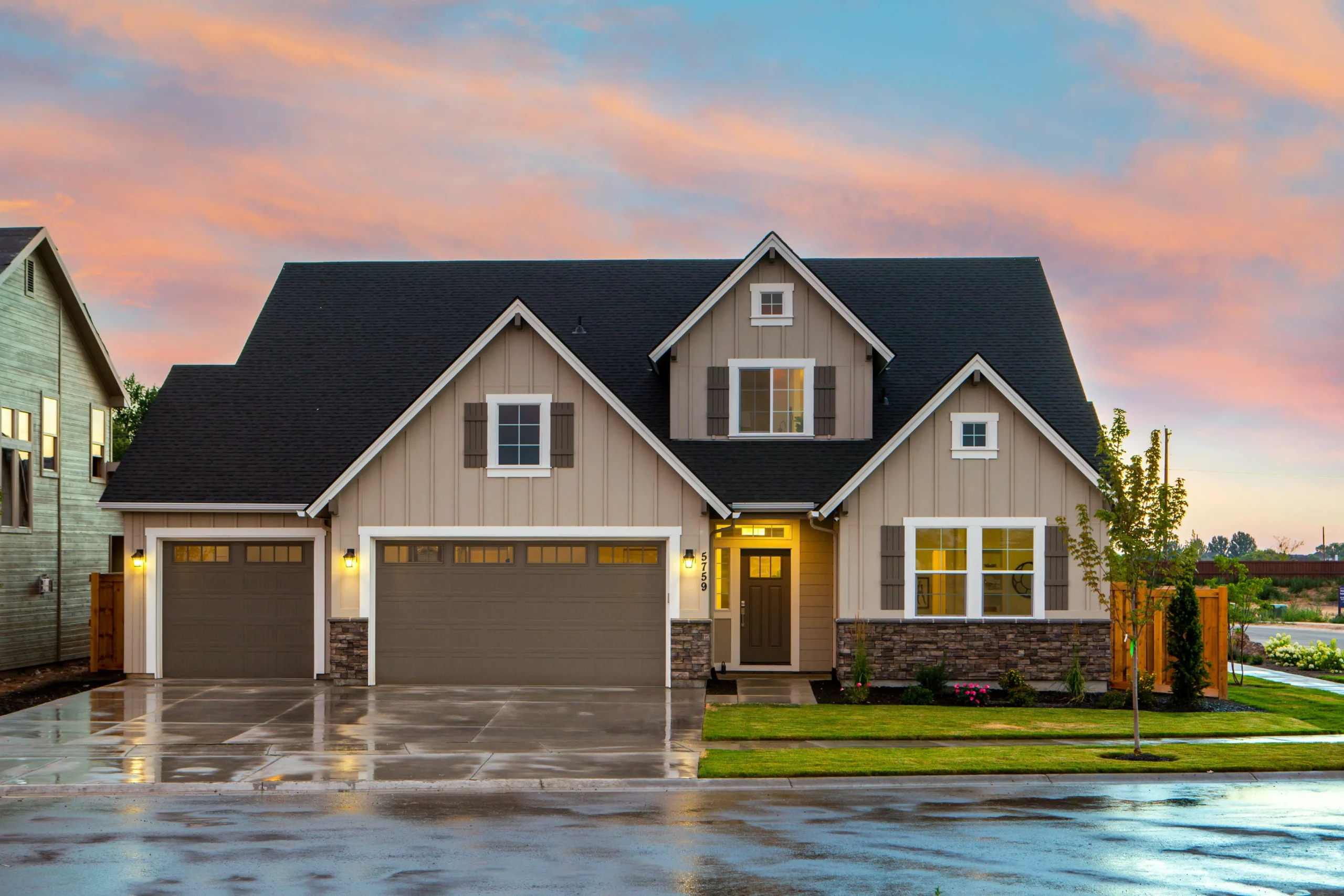 Modern suburban home with a stone accent, double garage, and lush landscaping, set against a colorful sunset sky.