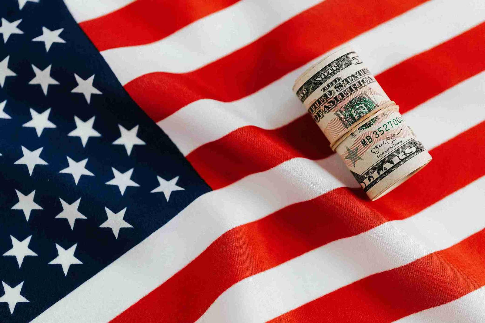A rolled bundle of U.S. currency resting on a draped American flag, symbolizing patriotism and financial themes.