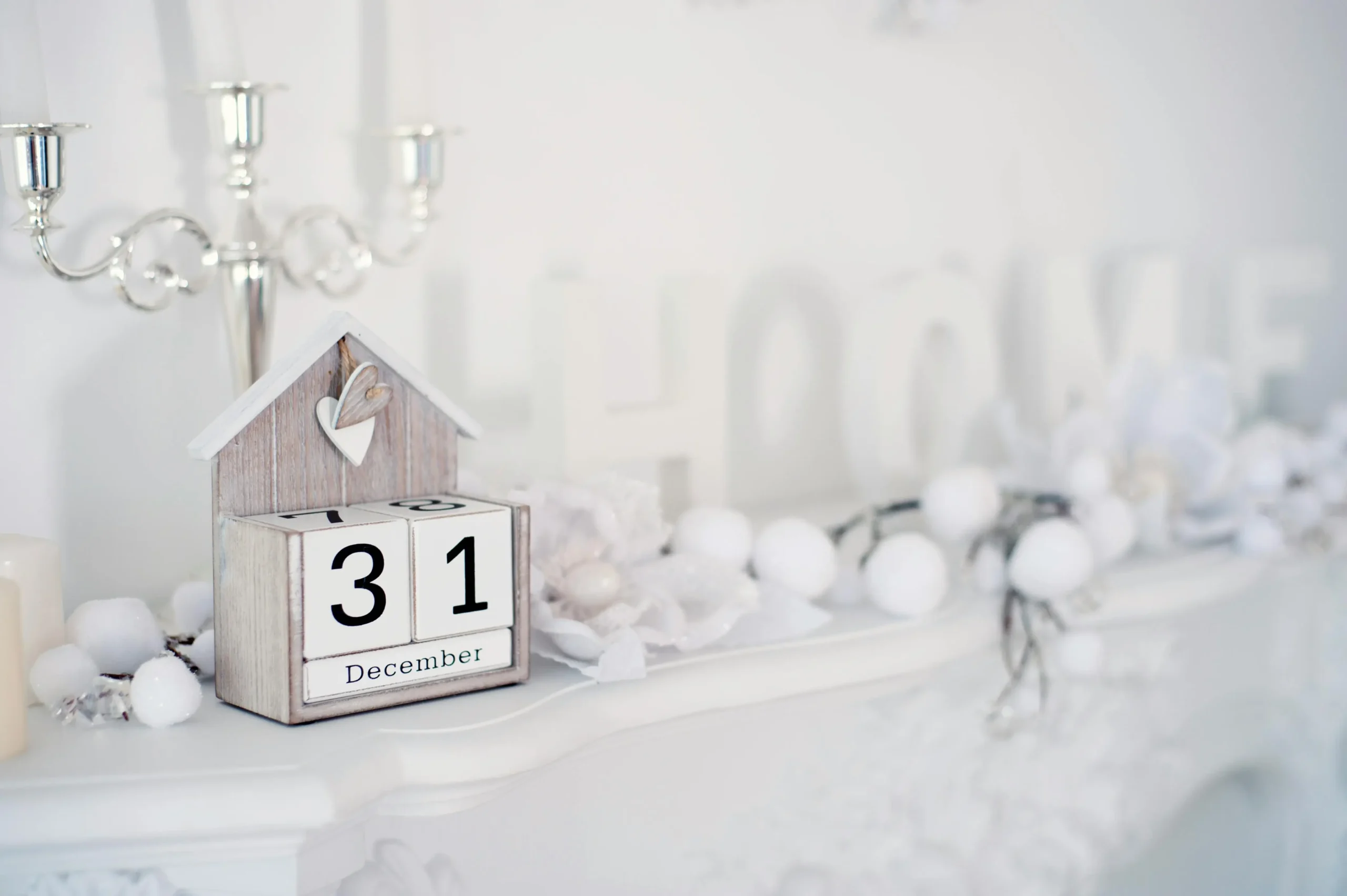 A festive mantelpiece featuring a calendar displaying December 31, decorated with white ornaments and a cozy home theme.