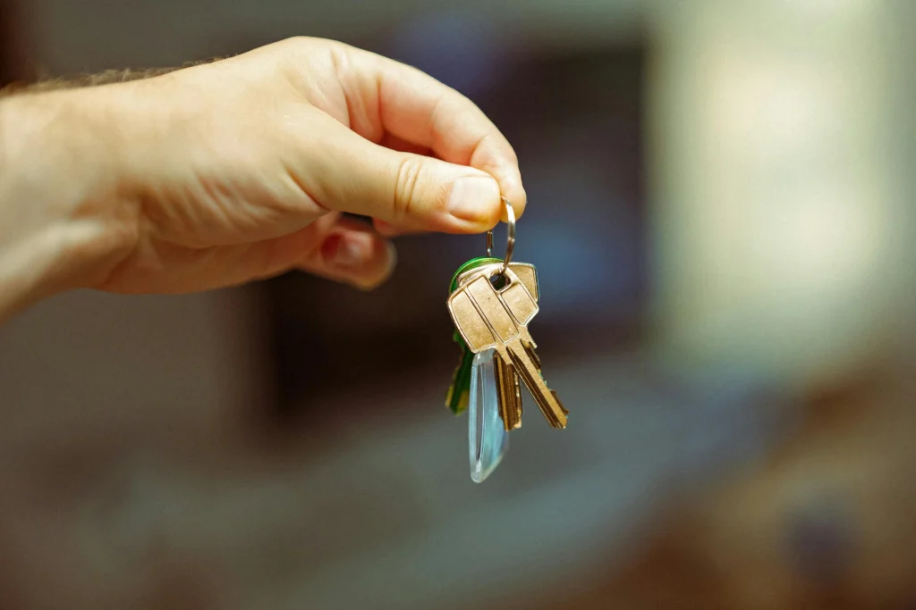 A hand holding a set of keys on a keyring, featuring several gold and silver keys against a blurred background.