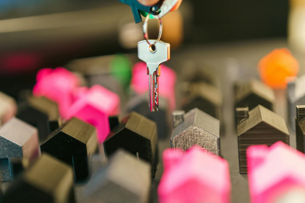 A hand holding a key above colorful mini house models, highlighting themes of homeownership and real estate.