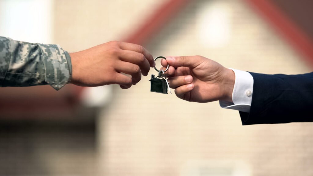A military personnel and a businessman exchange house keys, symbolizing a property transfer.