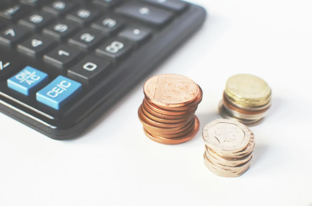 A close-up of a calculator beside neatly stacked coins in various denominations, representing budgeting or financial planning.
