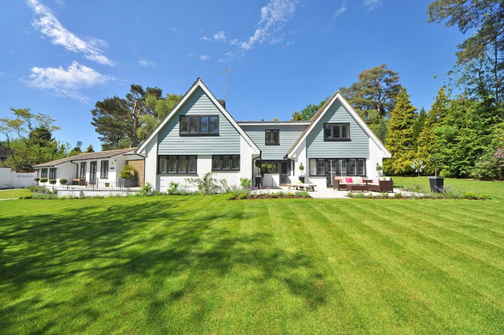 A modern two-story house with a sloped roof, surrounded by lush green grass and trees, under a clear blue sky.