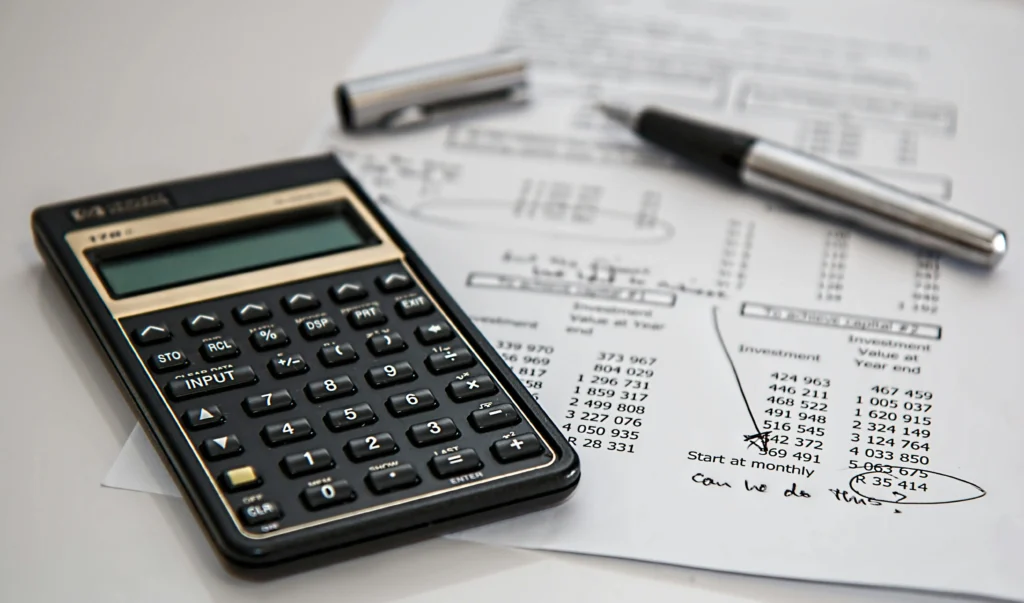 A calculator and a pen rest on financial documents filled with calculations and notes, including investment values and queries.