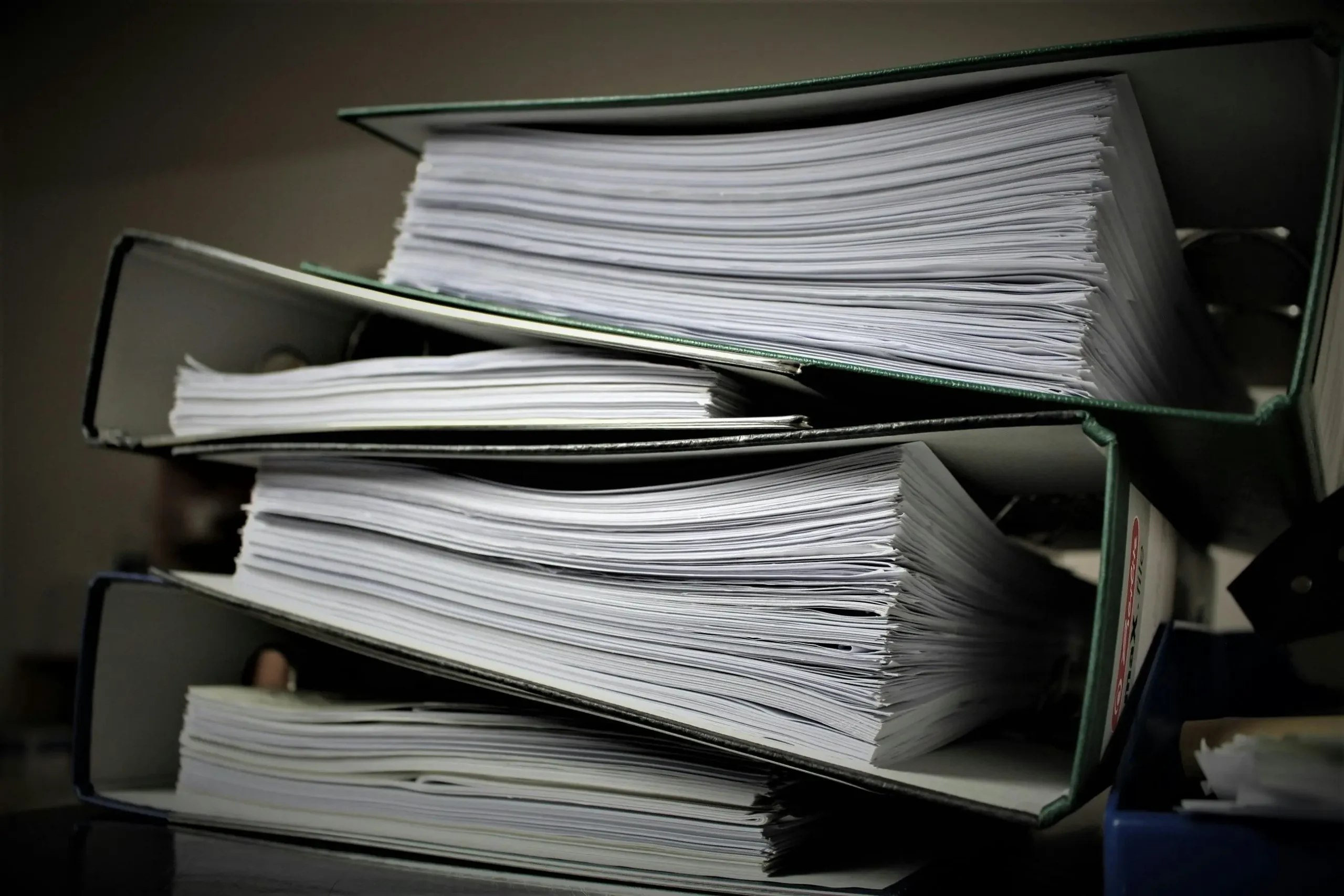 A stack of three green binders filled with neatly organized papers, resting on a dark surface, with soft background lighting.