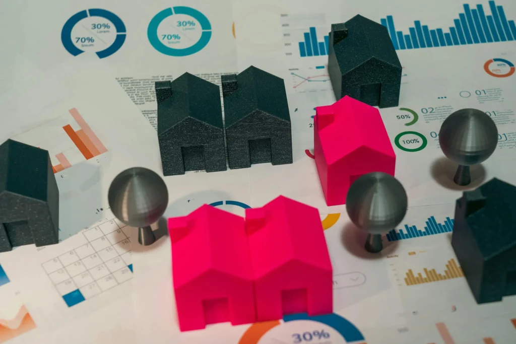 Colorful house models in pink and gray are placed on financial charts and graphs, depicting real estate data and statistics.