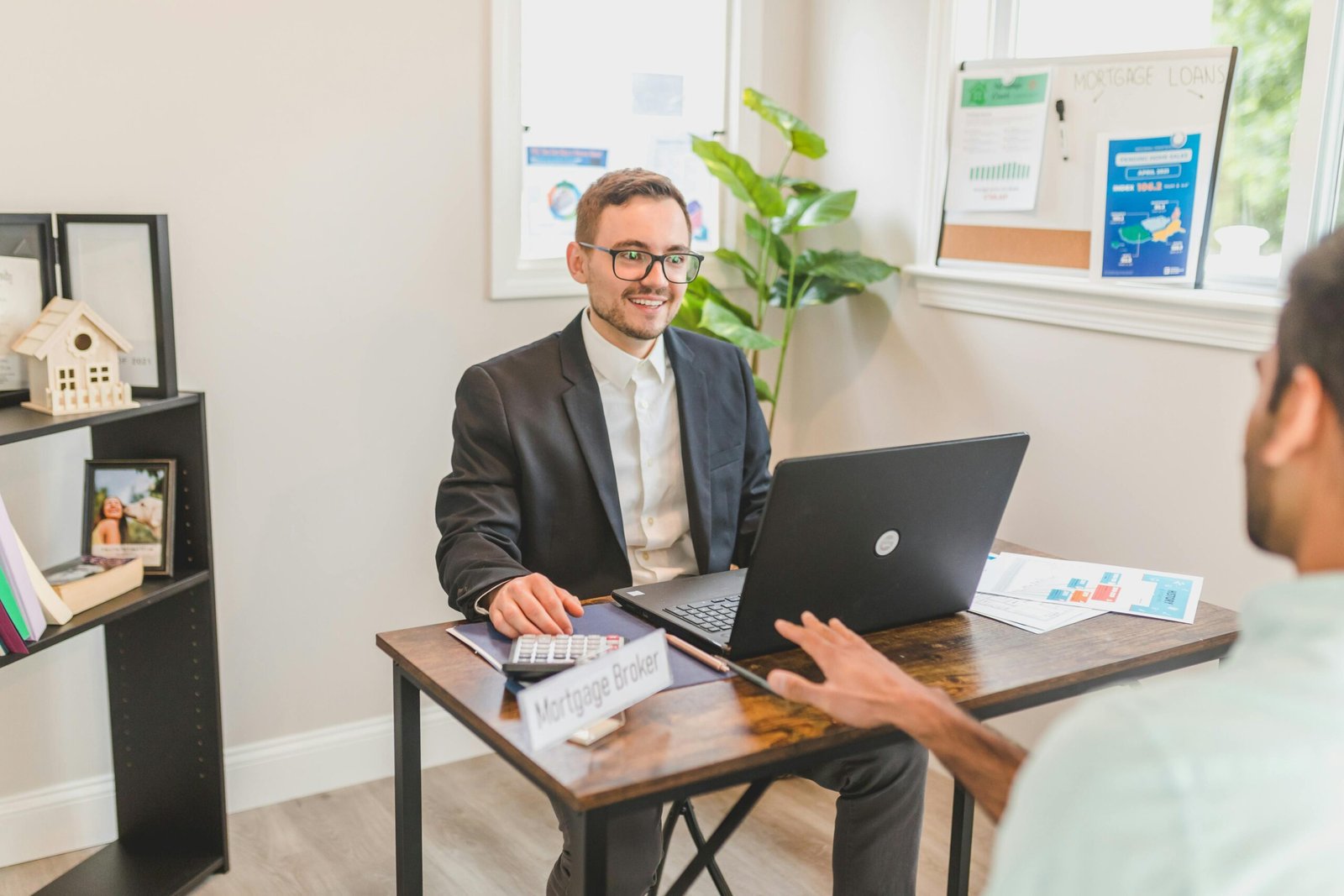A professional discussion at a desk featuring a mortgage broker with a laptop, papers, and calculator, focused on client needs.