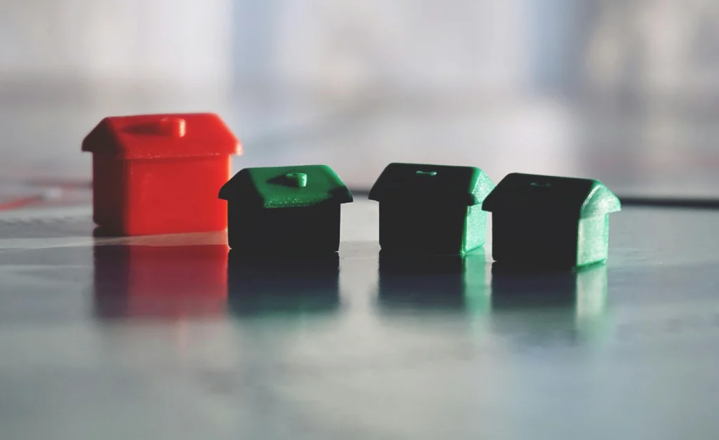 A close-up of four miniature house tokens: one red and three green, reflecting light on a smooth surface.