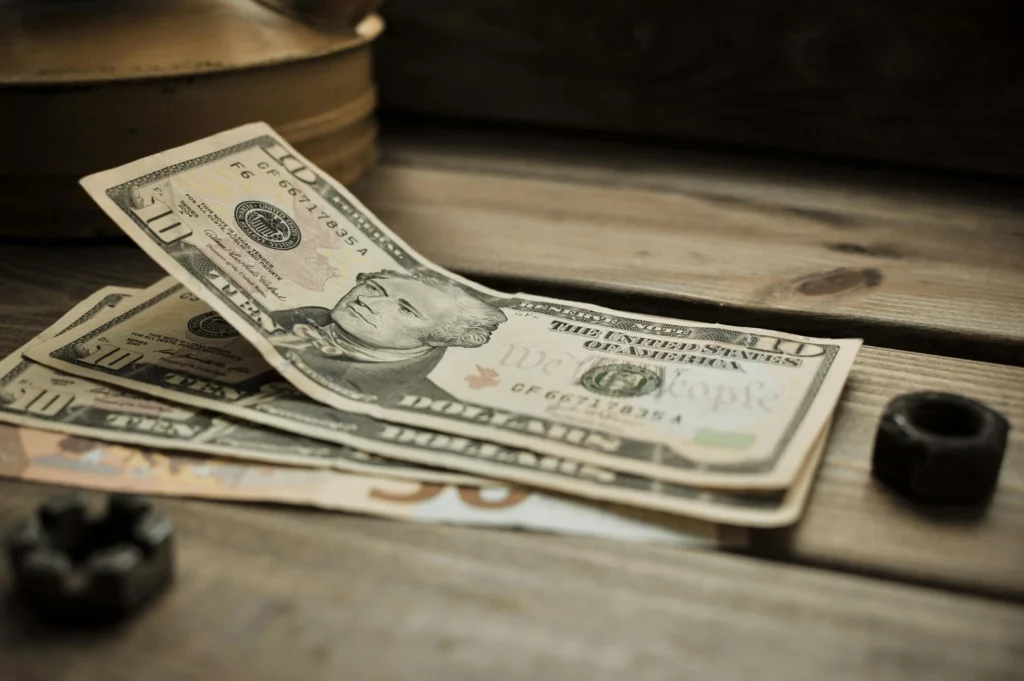 A close-up view of various U.S. banknotes resting on a wooden surface, near a small metal nut.